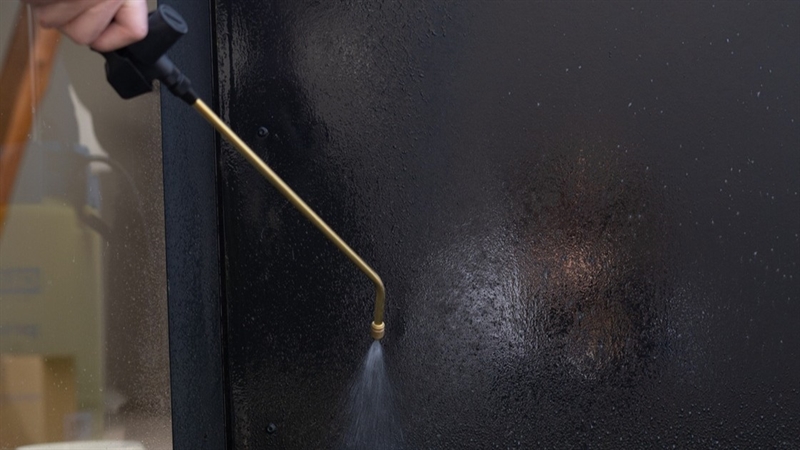 Påføring af Urban-Hald Afrenser på sort facadebeklædning med pumpesprøjte