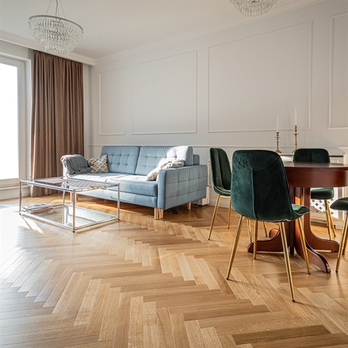 Lækkert sildebensparketgulv med facet kanter i herskabelig stue med lysblå sofa, lysekroner og mørkegrønne spisebordstole